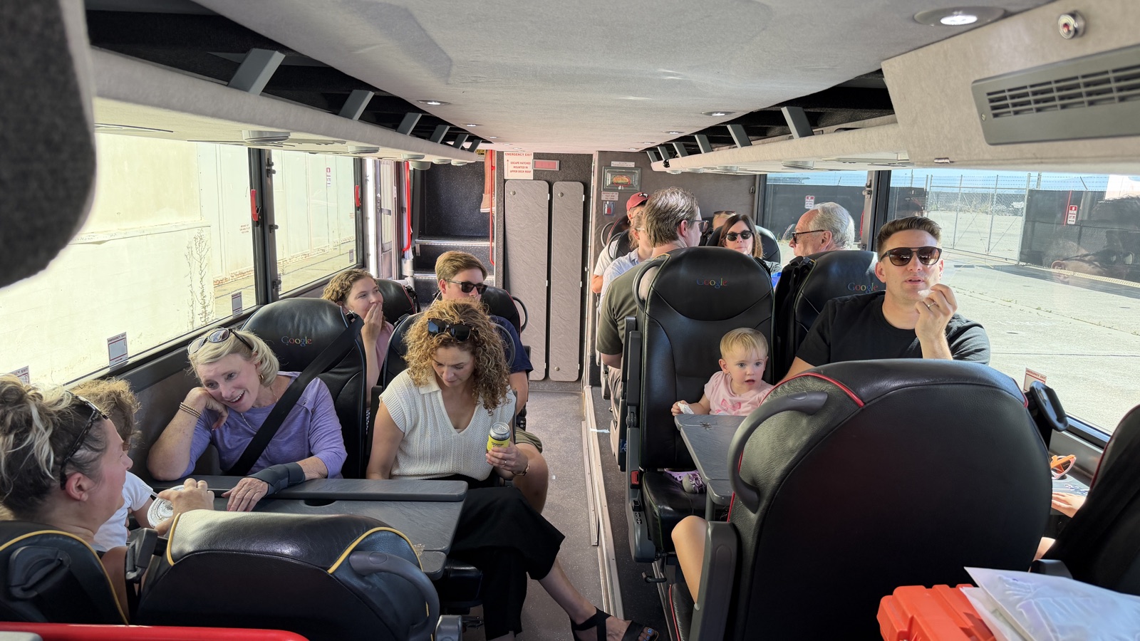 Inside the lower deck of the double decker, families settling into their seats before the bus pulls out, the stairs to the upper deck at the back.