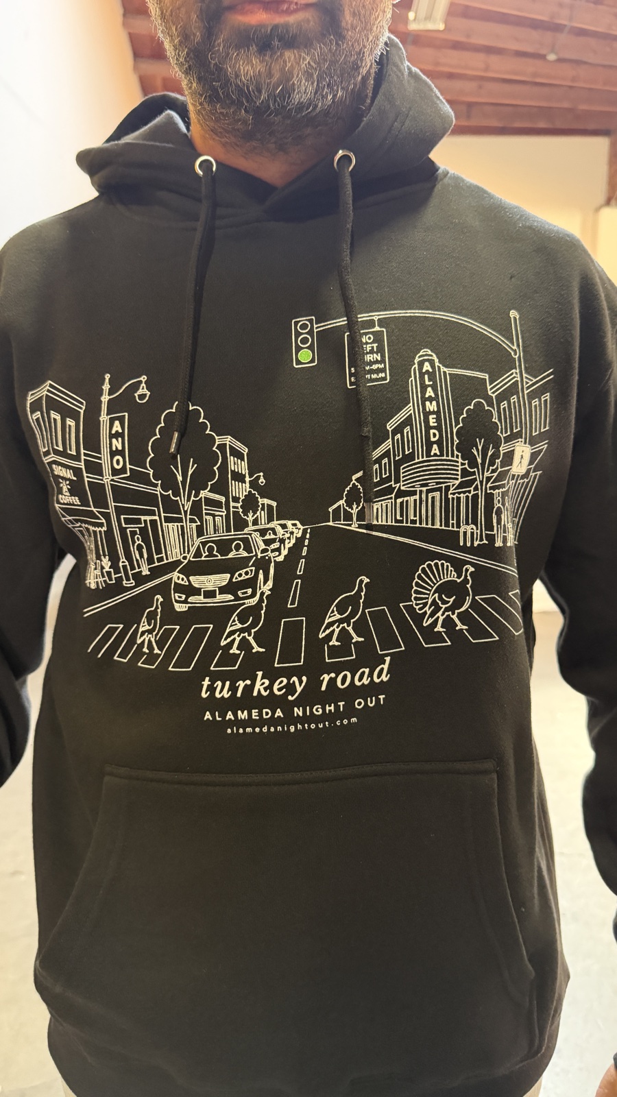 The Turkey Road Hoodie in black: white line art of the Alameda theater and turkeys crossing the street